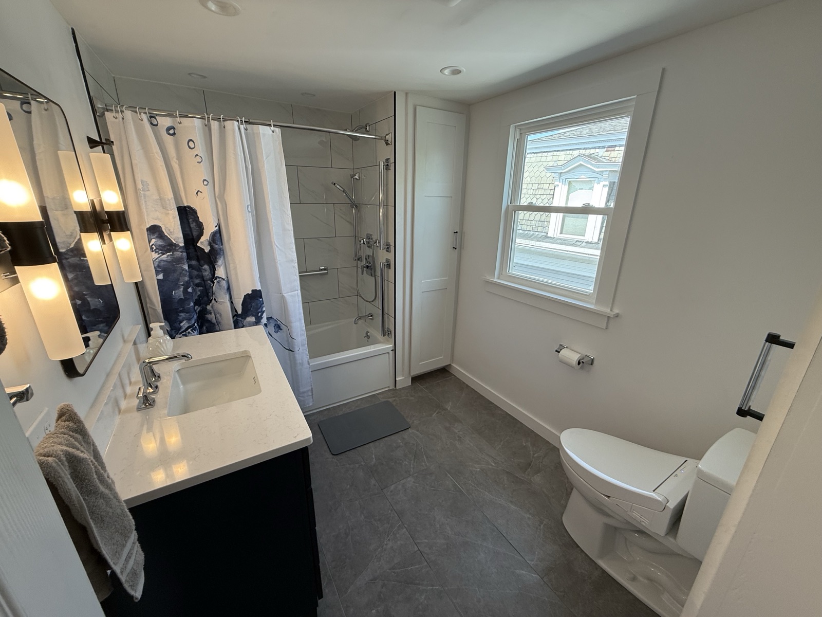 Renovated bathroom with a tiled tub and shower, a dark vanity, and a toilet