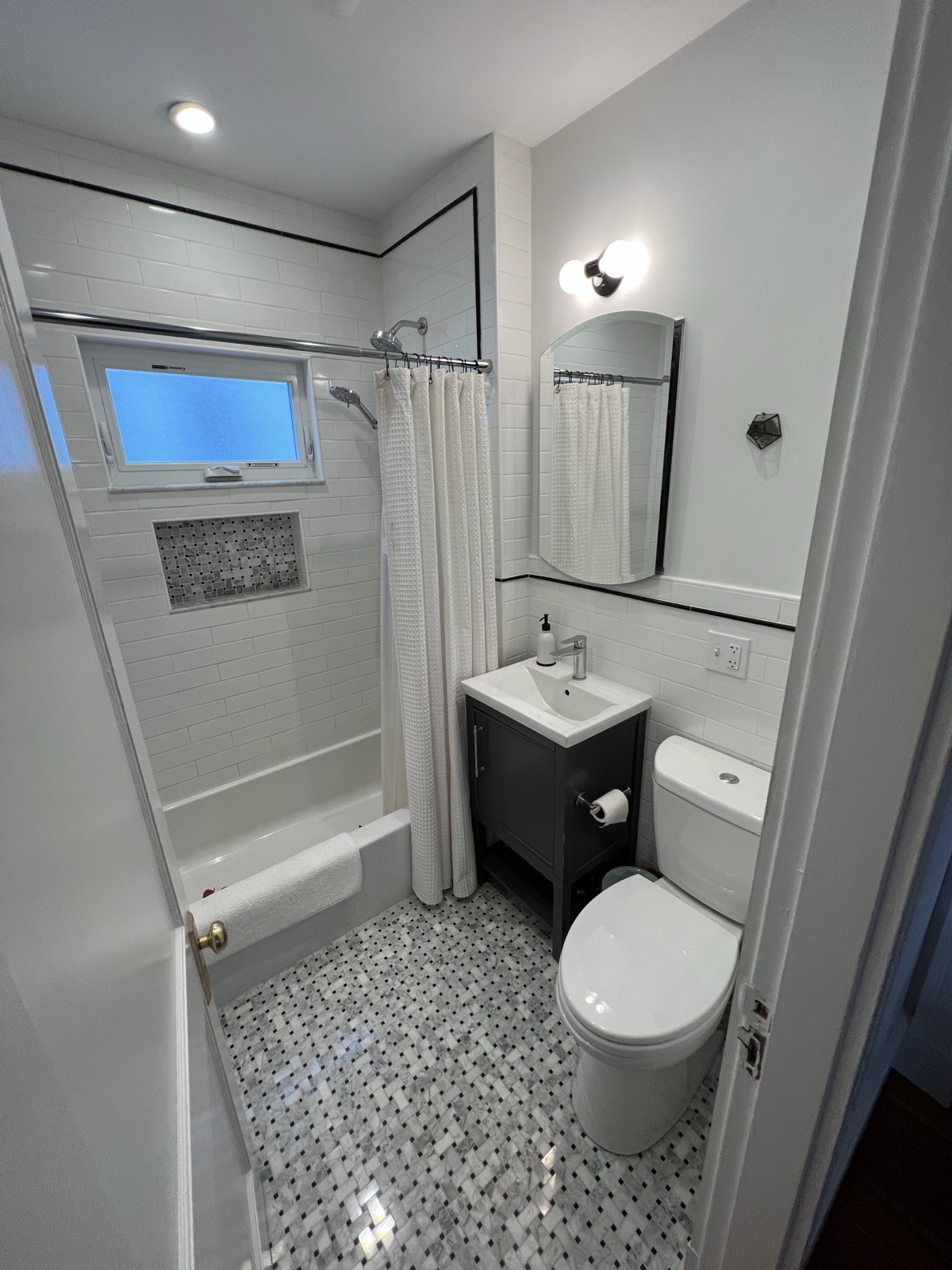 Compact full bathroom with a subway-tiled tub surround, a marble basketweave floor, a small vanity, and a toilet
