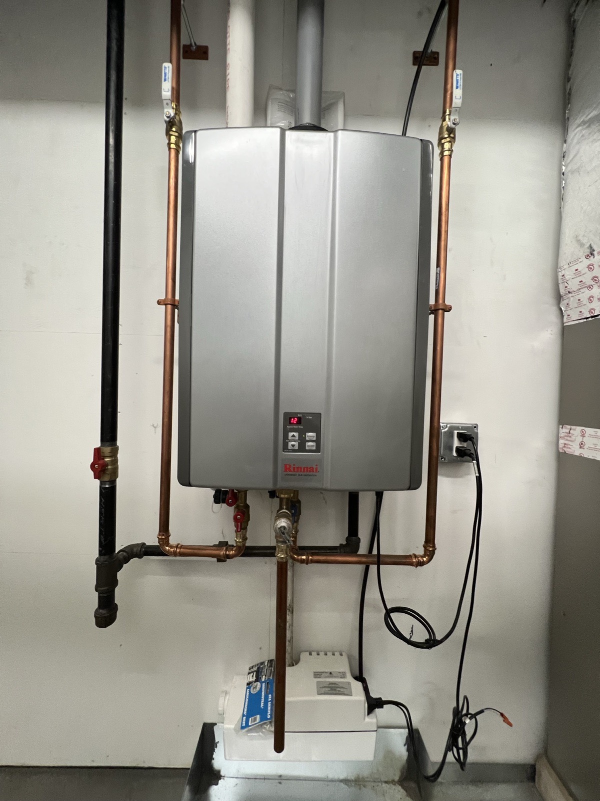 A single Rinnai tankless water heater with new copper supply lines, isolation valves, and a condensate pump