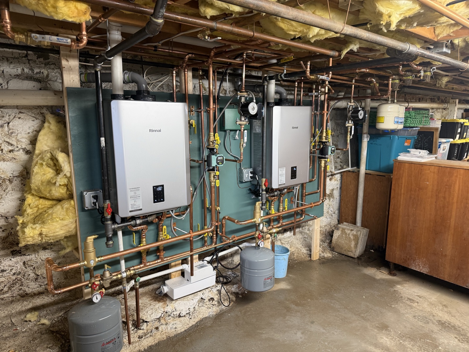 Two wall-mounted Rinnai tankless water heaters on a shared copper manifold with circulators and expansion tanks