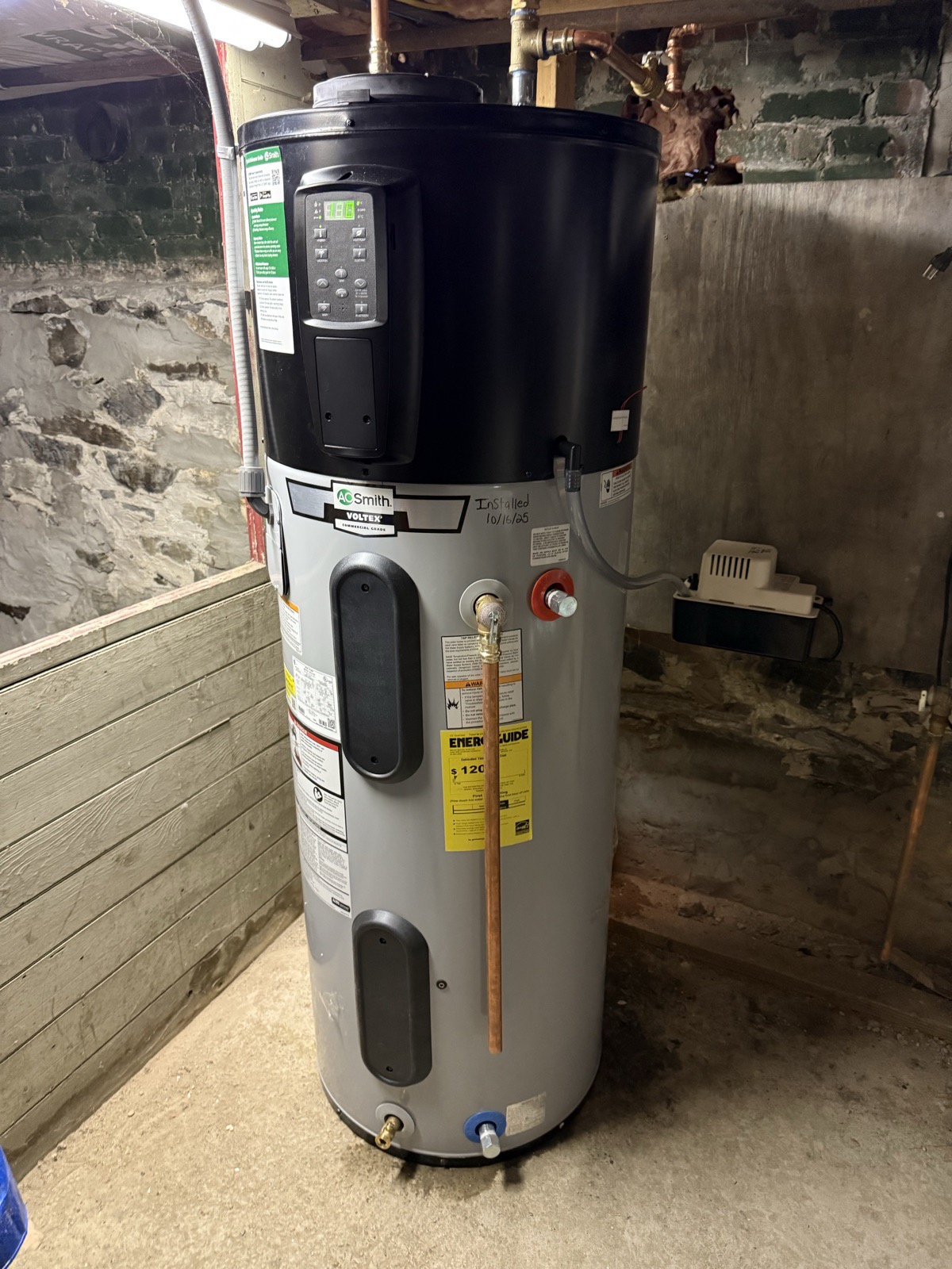 A. O. Smith heat-pump water heater installed against a stone foundation wall with a condensate pump